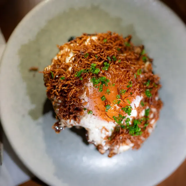 Crisp noodles topped with a confit egg yolk and sliced spring onion at Mirin